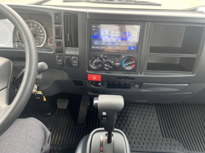 Dashboard view of a 2023 Chevrolet 4500 HD flatbed truck showing steering wheel, digital display, center console with climate controls, gear shifter, and textured floor mat.