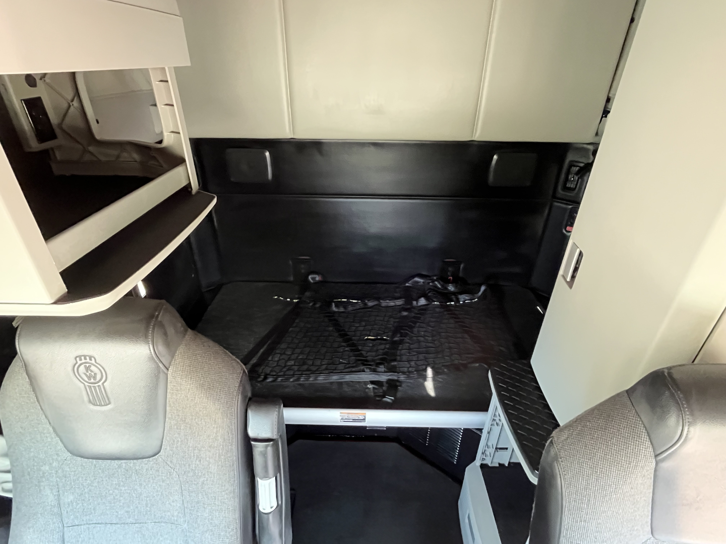 Kenworth T680 sleeper cab interior showing cargo area with rear cab and storage shelves.