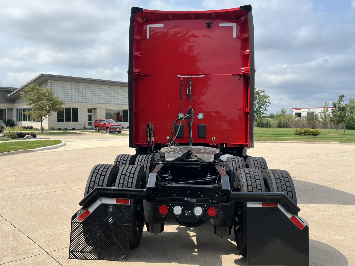 Kenworth T680 rear view showing fifth wheel, dual rear axles, and mud flaps with red sleeper cab in background.