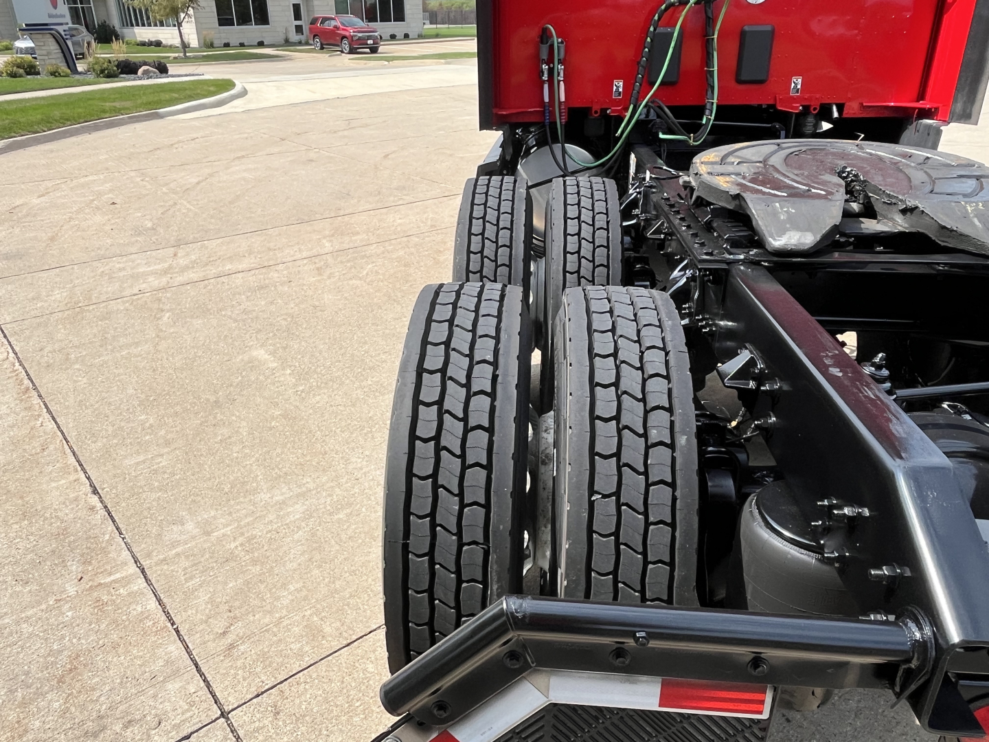 Dual rear axles of a Kenworth truck chassis with visible tires and frame in view; part of a red cab is top; no identifying text legible on components.