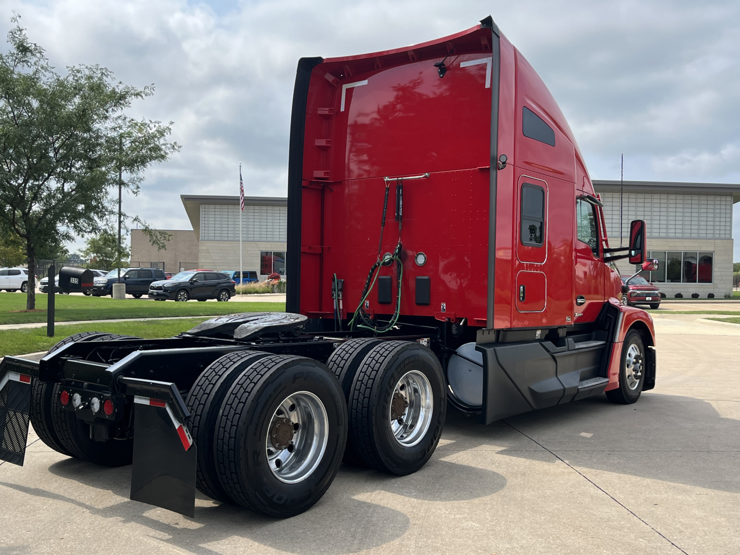 Kenworth T680 conventional sleeper tractor from rear-left angle showing red cab and dual rear axles with chrome wheels and hitch area.