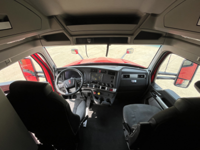 Kenworth T680 cabin interior viewed from behind the seats; dashboard with steering wheel, center console, and overhead storage visible.