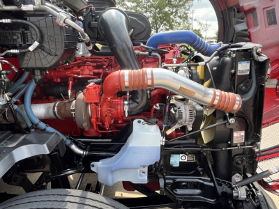 Kenworth T680 engine bay with red engine, orange turbo inlet, blue coolant reservoir, and various hoses and components visible.