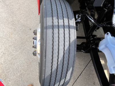 Kenworth truck front wheel area with dual rear wheel hub, tire treads visible, and suspension components.