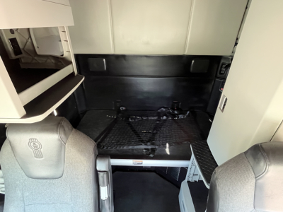 Kenworth T680 sleeper cab interior showing cargo area with rear cab and storage shelves.
