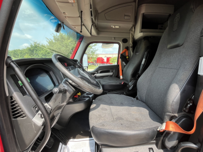 Kenworth T680 cab interior showing driver seat and steering wheel with dashboard; view of passenger seat and overhead storage, fabric seats.