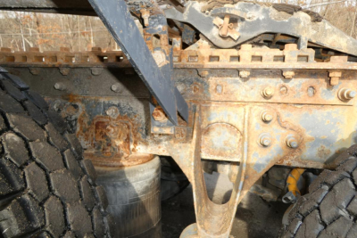 Truck chassis frame and suspension components with rust and dual tires visible under a dump of components