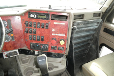 Truck cab dashboard with red panel showing various switches and controls, steering wheel on left, gear shifter visible.