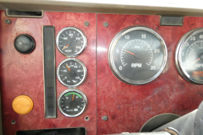 Dashboard panel of a 2004 International 9400 showing gauges and switches. Visible text includes 'RPM' on the large tachometer, and volt/oil/air gauges with numbers. There is a yellow/orange push button labeled 'RUN' and a black dial with 'O