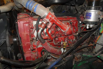 Engine bay of a 2004 International 9400 showing red diesel engine with hoses, metal piping, and a blue coolant hose; various connectors and black belts visible.
