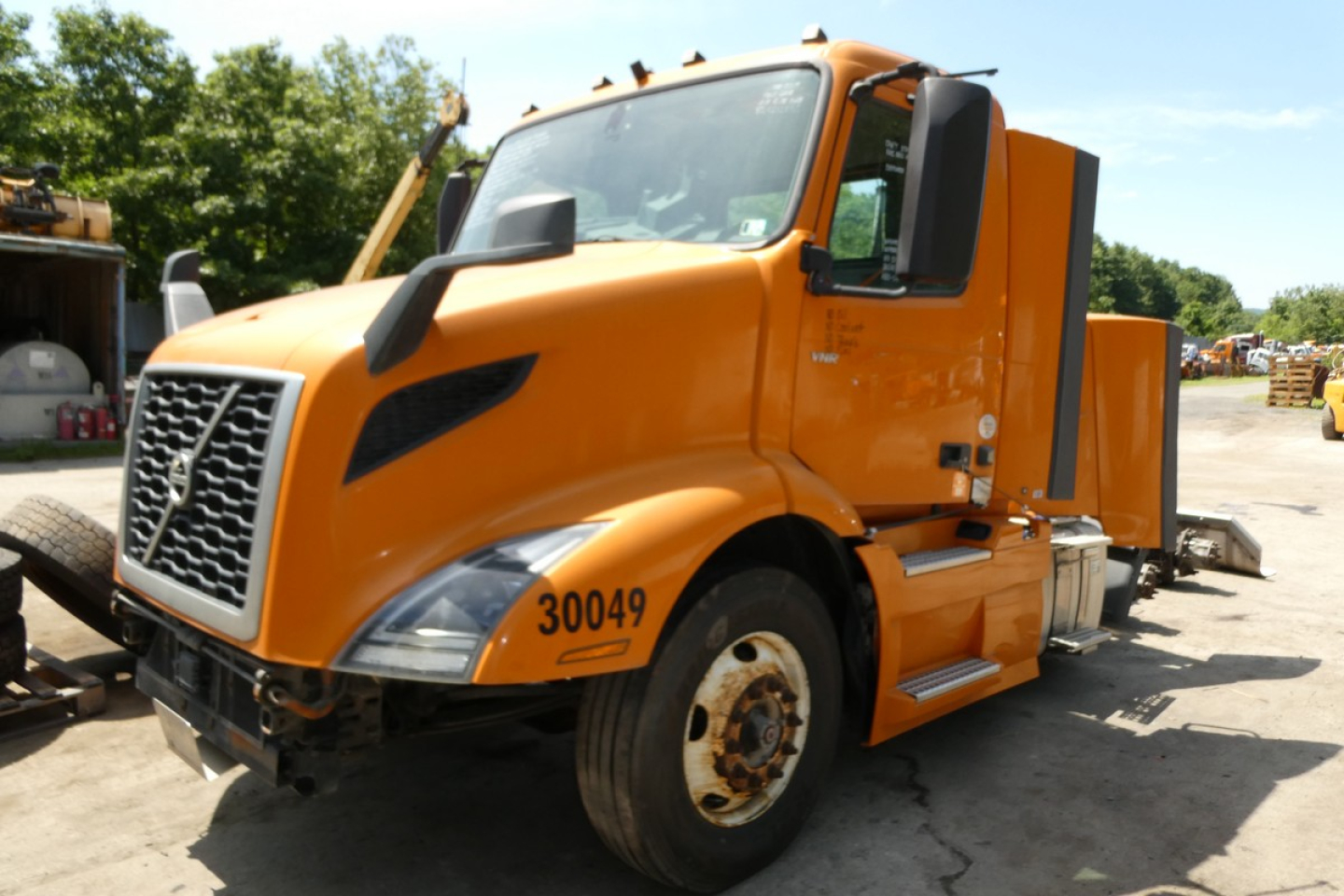 Volvo VNR64T300 box truck in orange, front-left view with VIN tag and stock number visible.