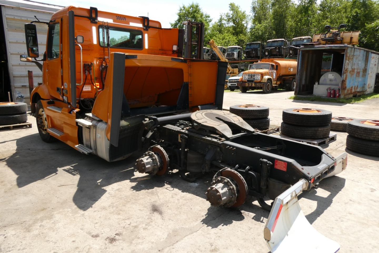 Volvo VNR64T300 cab with chassis exposed and orange body, front view showing wheels and drivetrain, used commercial truck.