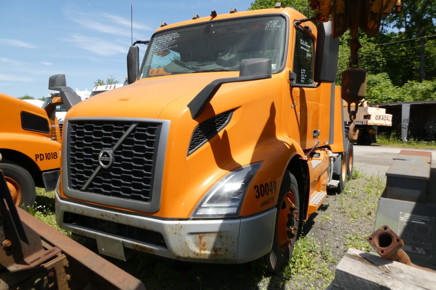 Volvo VNR64T300 conventional daycab truck in orange, front-left view showing grille, headlights, and side cab numbers.