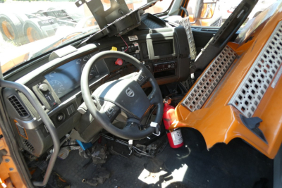 Volvo VNR truck cab interior showing steering wheel and dashboard with orange exterior panels and a fire extinguisher.