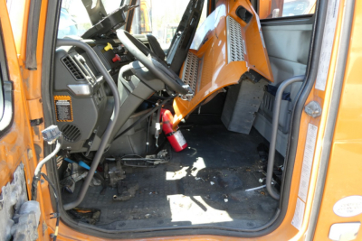 Cab interior of a 2019 Volvo VNR64T300 daycab truck with orange exterior, showing steering wheel, dashboard, and driver's seat area.