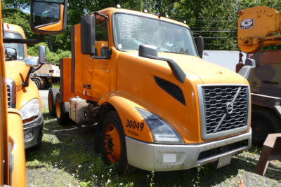 Volvo VNR64T300 truck in orange with front grille and large bumper, side number 30049 visible.