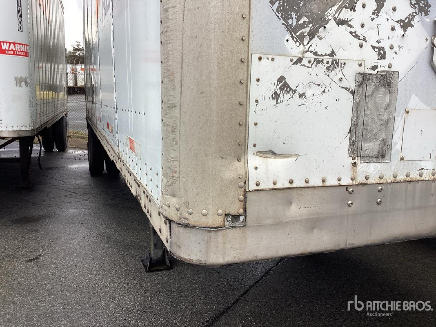Trailer corner showing riveted metal exterior with weathered white paint and a black rubber corner guard.