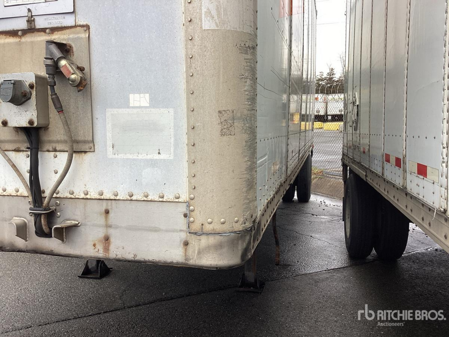 Trailer rear view showing bumper, reflective tape, and support legs of a used Wabash trailer with visible side of another trailer nearby.