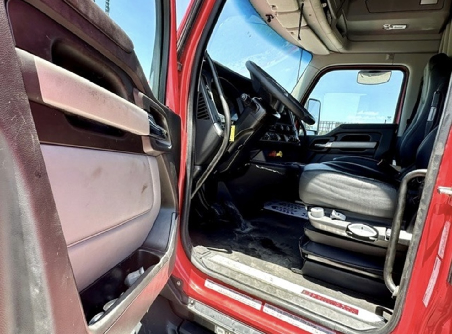 Kenworth T680 truck cab interior and open driver door showing seat and steering wheel.