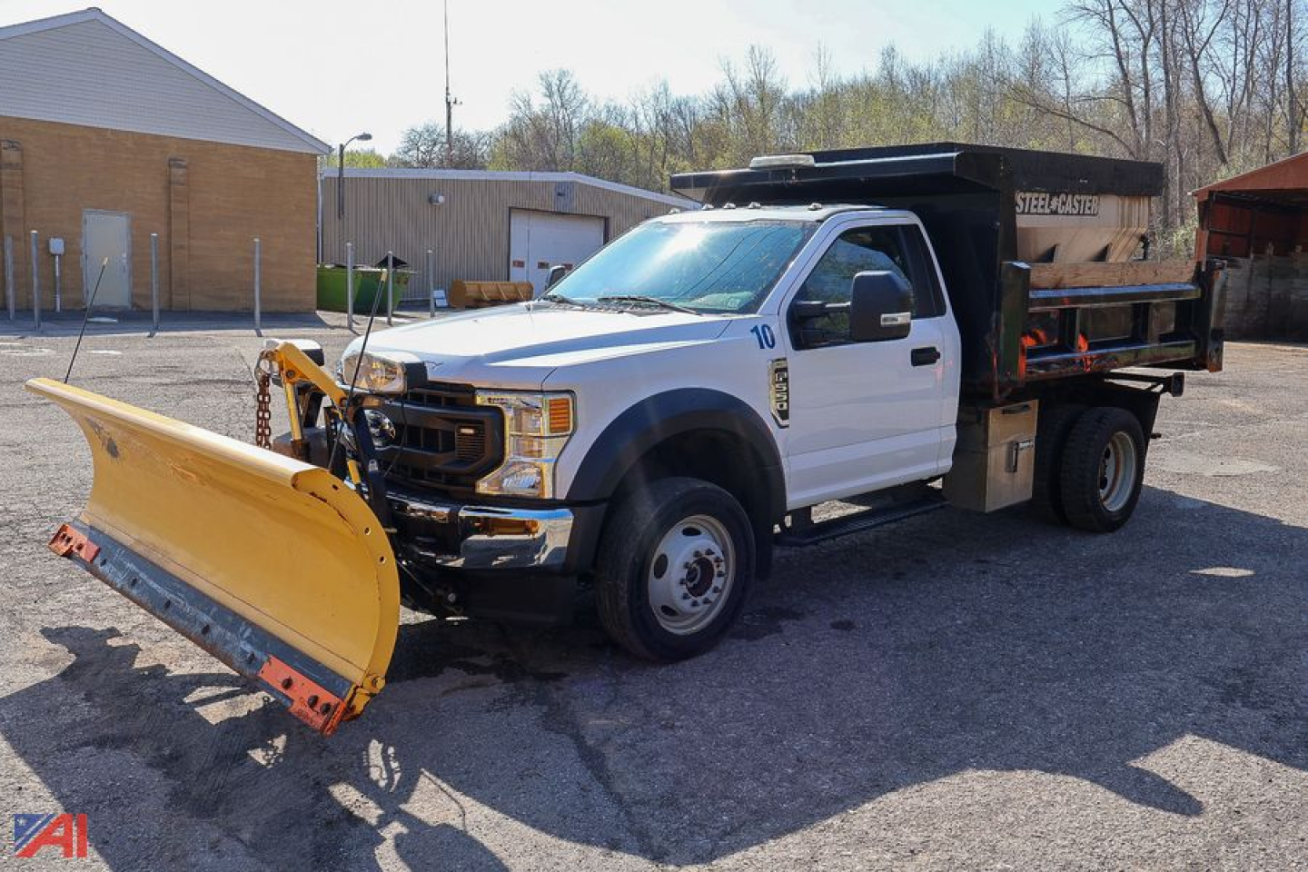 Ford F-550 dump truck with front plow and spreader in a parking lot, white cab, yellow plow, steel dump bed