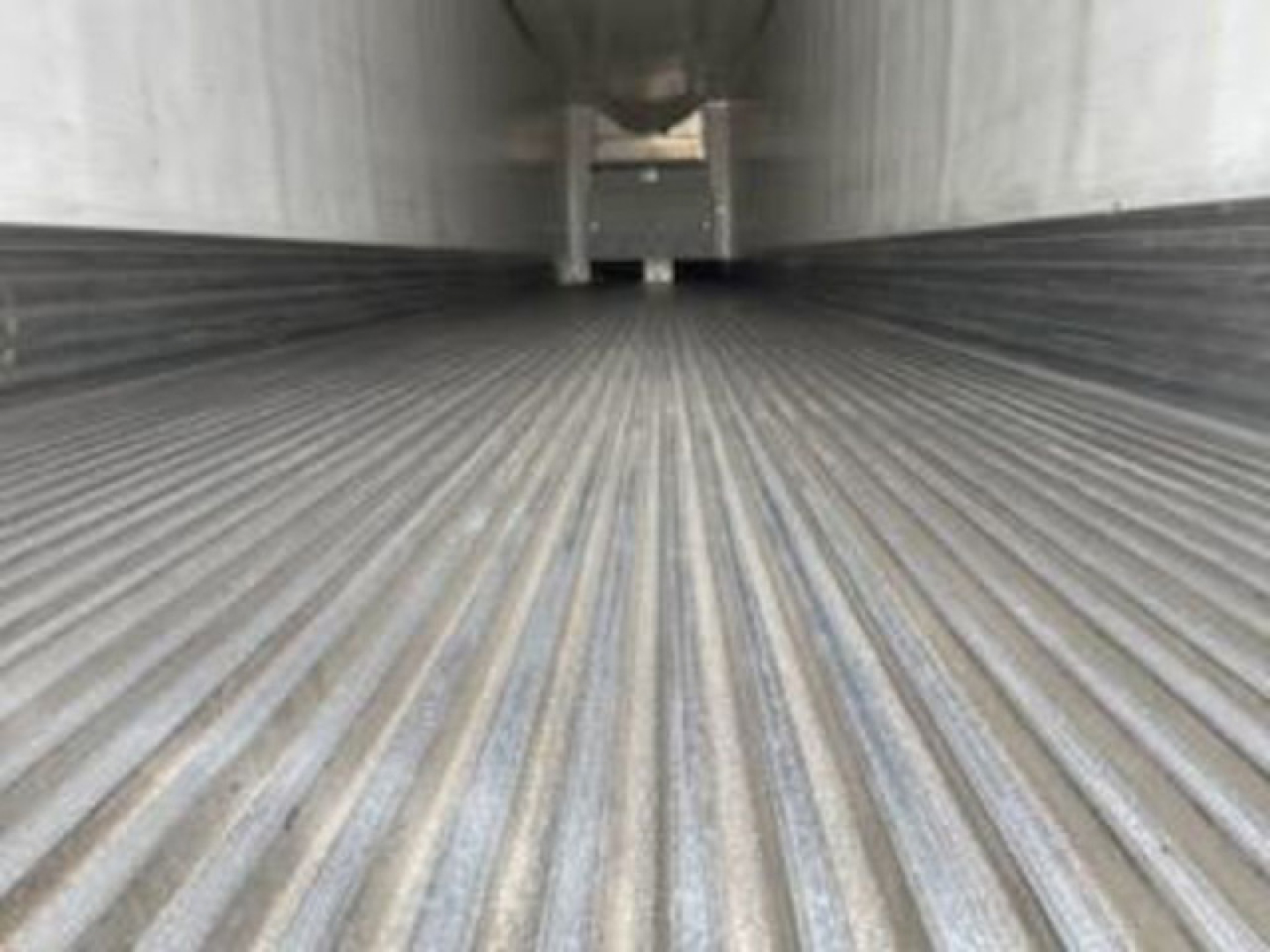 Interior of a refrigerated trailer cargo area with corrugated metal floor and vertical walls extending into the distance.