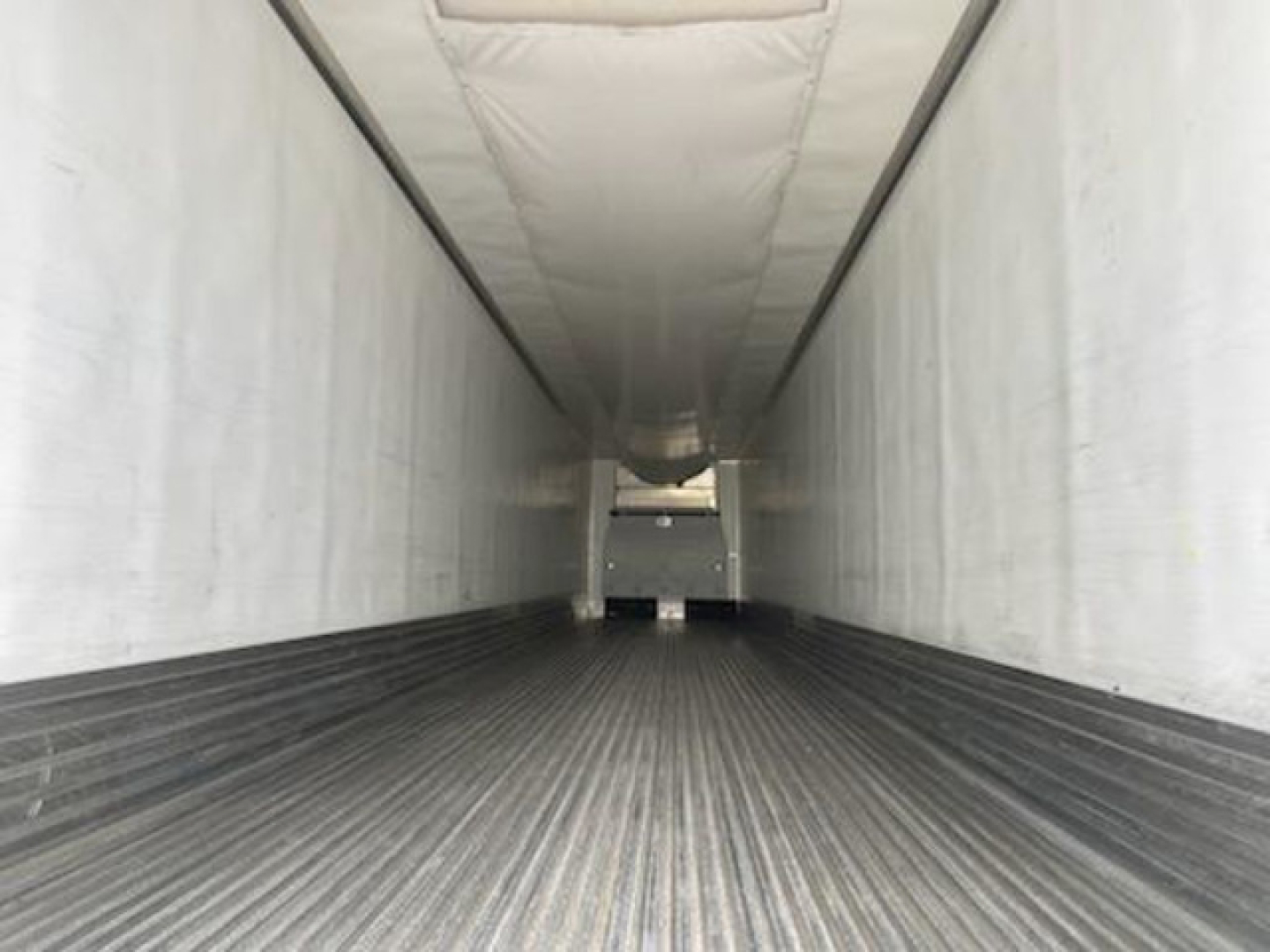 Inside view of a refrigerated trailer showing long narrow cargo area with ribbed floor and white interior walls.