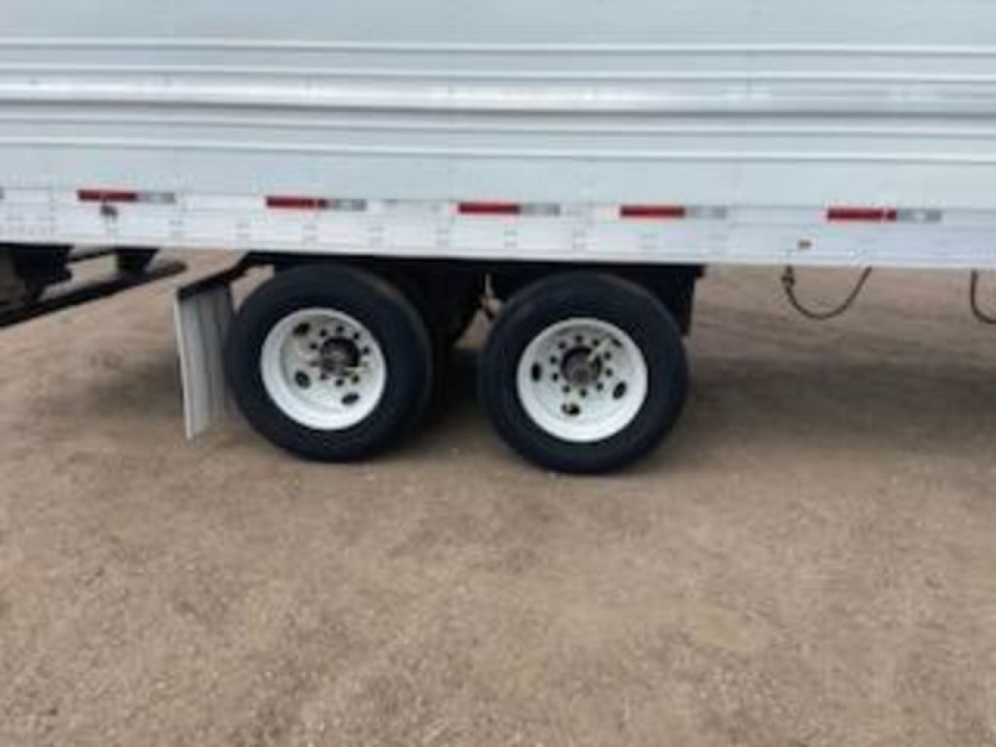 Utility reefer trailer showing dual rear wheels under a silver cargo box with white rims.