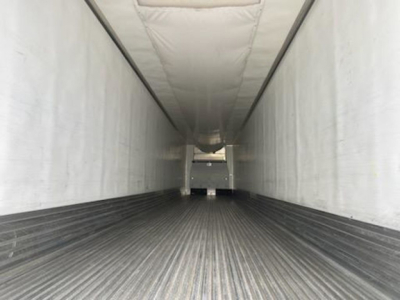 Inside view of a refrigerated trailer showing long narrow cargo area with ribbed floor and white interior walls.