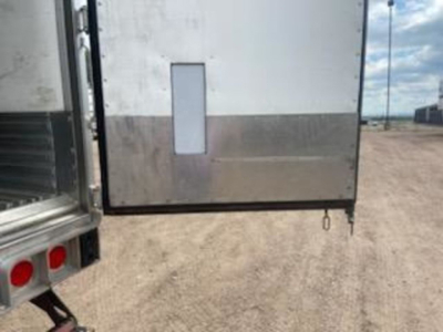 Rear of a refrigerated trailer with lower reflective metal panel, small vertical door handle and a retractable latching ring near the bottom corner.