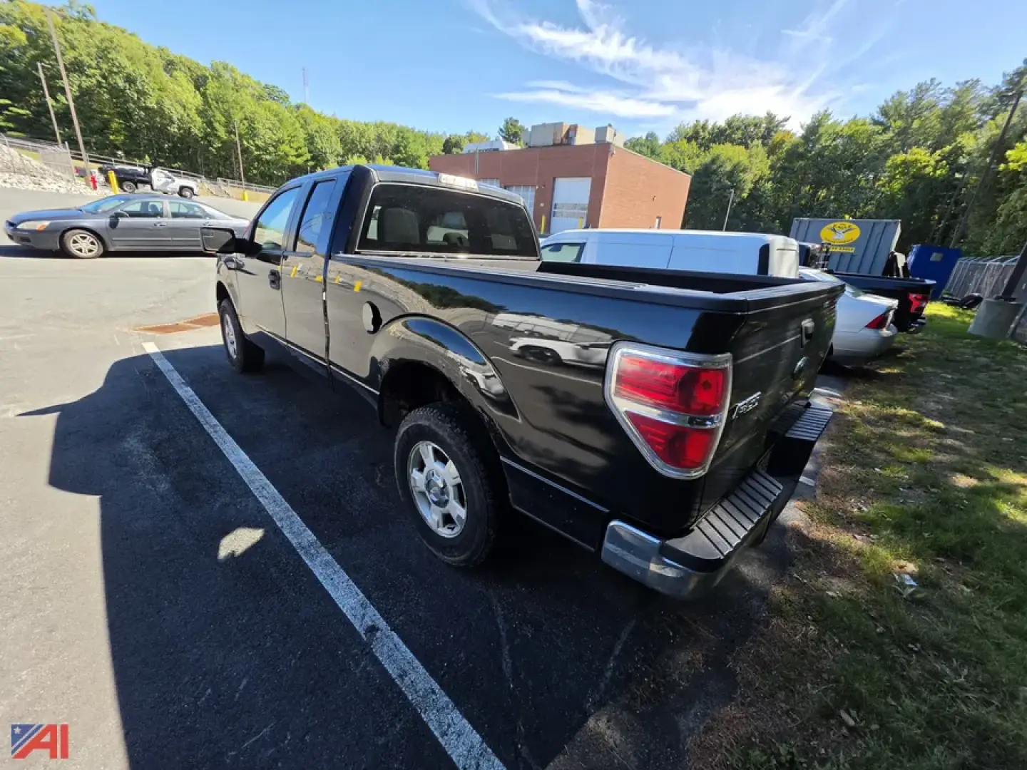 2013 Ford F-150 pickup truck in a parking lot, rear-right view, black color, 4x4, tailgate down, bed cover visible, dealership lot background.