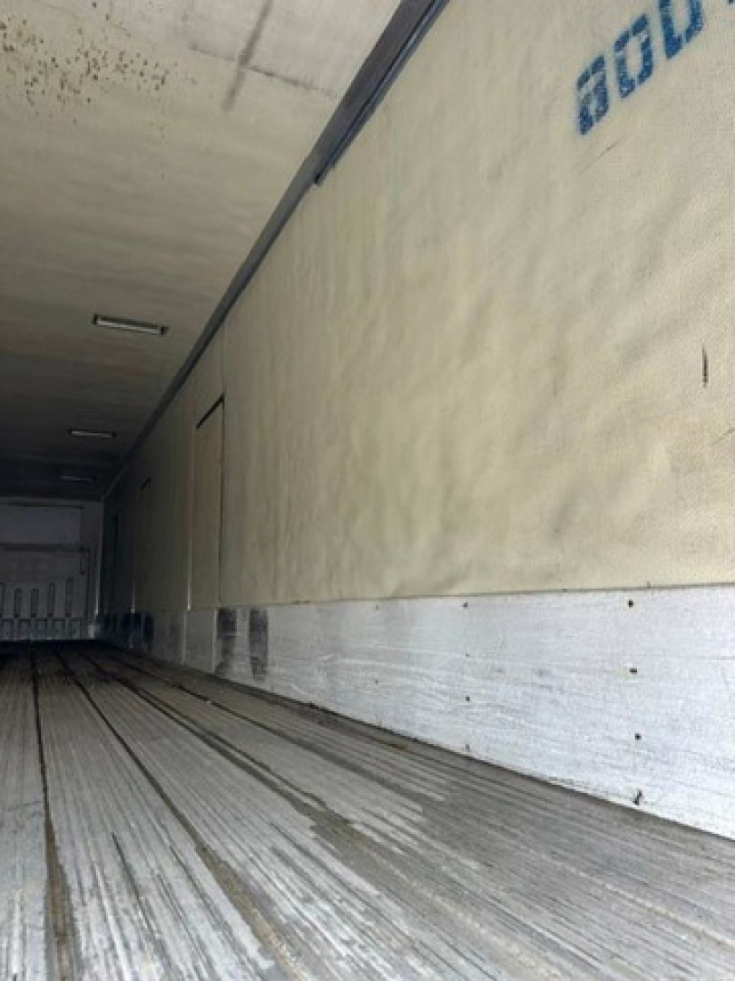 Inside view of a refrigerated trailer, metal floor with rails, insulated sidewall with partial blue text and a door at far end.