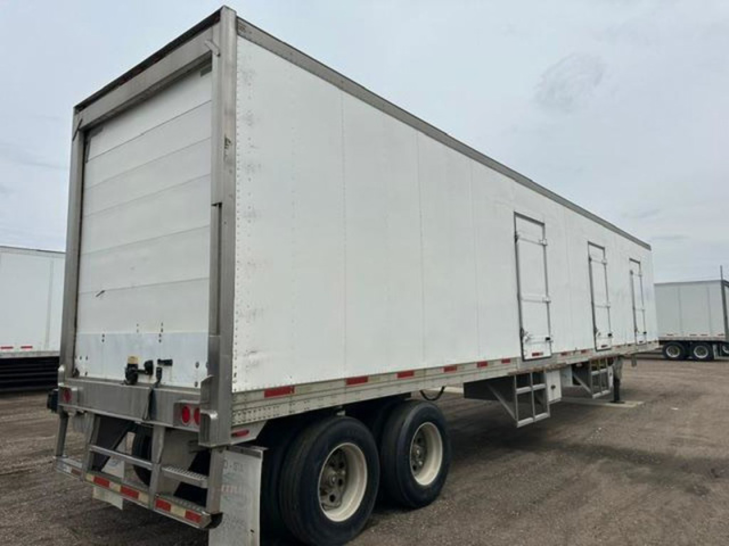 Utility reefer trailer in profile view showing dual rear axles and closed white side with doors, aluminum frame, stock body, trailer hitch, and reflective tape.