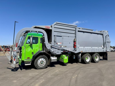 Peterbilt 520 garbage truck with green cab and gray body, side view showing dump body and rear wheels.