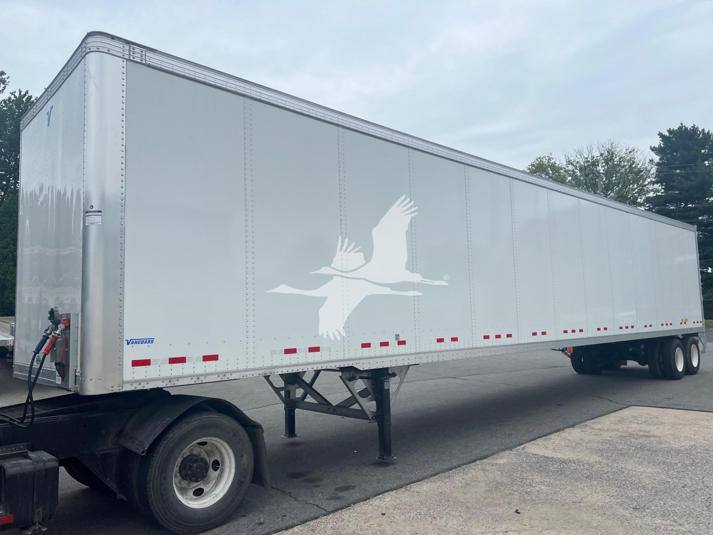 Vanguard VXP trailer showing side view with white exterior, logo of a flying bird, and red reflective strips along lower edge.