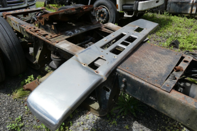 Truck chassis frame with metal steps and frontend bumper piece, rusted frame and exposed components from a Mack R600 truck, 1985 model year.