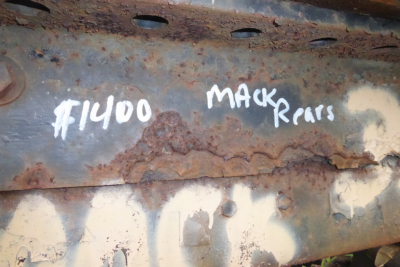 Surface of a rusty metal frame with chalked text reading 'F1400' and 'MACK' 'Rear'