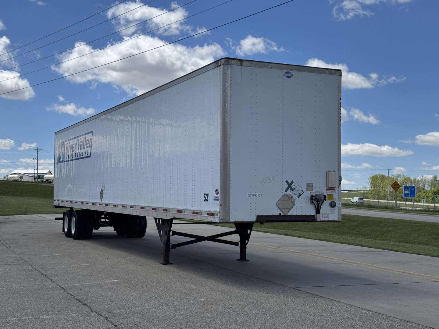 Trailer in a lot showing a white Utility trailer with raised legs and rear doors. Visible markings include 'Utility' logo on the side and various hazard stickers near the back.