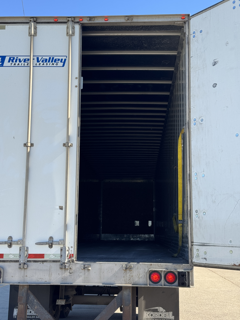 Trailer interior seen through open rear doors of a 2014 Utility 4000DX van trailer, empty ribbed metal interior, exterior shows River Valley trailers branding and rear lights visible.