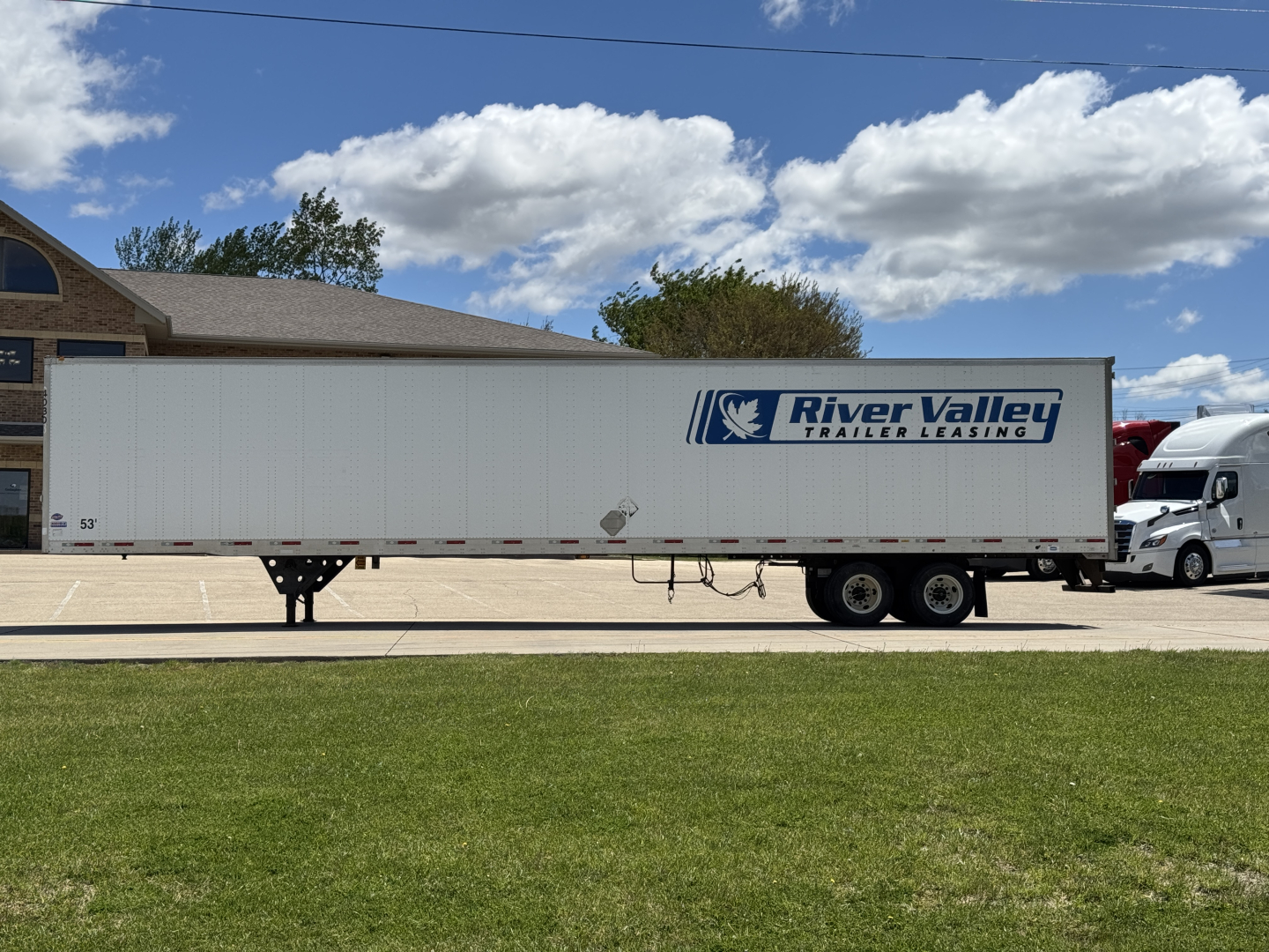 Trailer side view showing River Valley Trailer Leasing logo on a white utility trailer with tandem axles in a parking lot