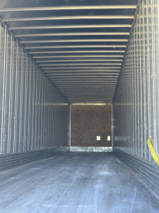 Trailer interior showing empty metal cargo space with ribbed walls and ceiling, rear door closed.