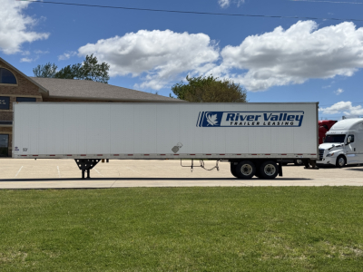 Trailer side view showing River Valley Trailer Leasing logo on a white utility trailer with tandem axles in a parking lot