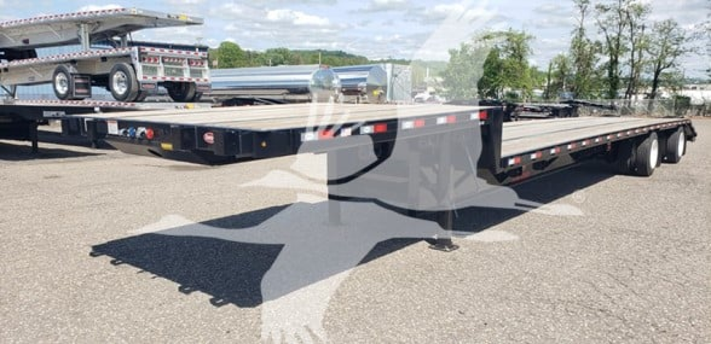 Flatbed trailer with low deck showing beavertail design and multiple axles, no visible branding text.