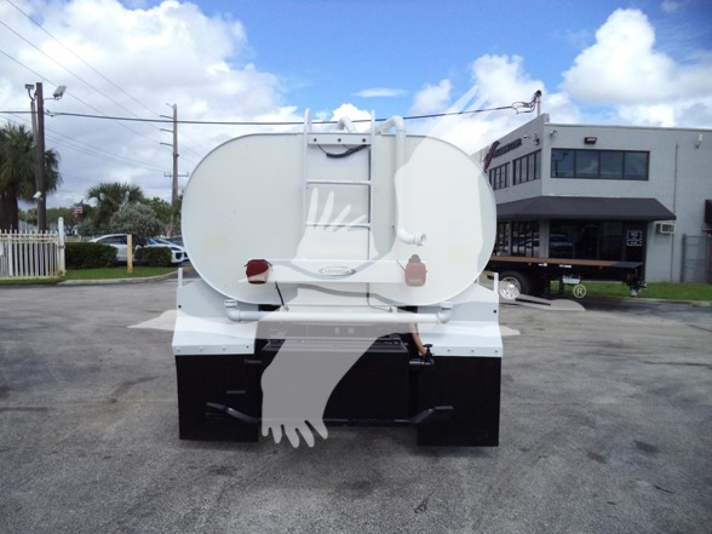 Rear view of a white 2017 Ford F650 truck with a large circular tank and a hanging cutout of a hand on the back. Clear blue sky with some clouds.