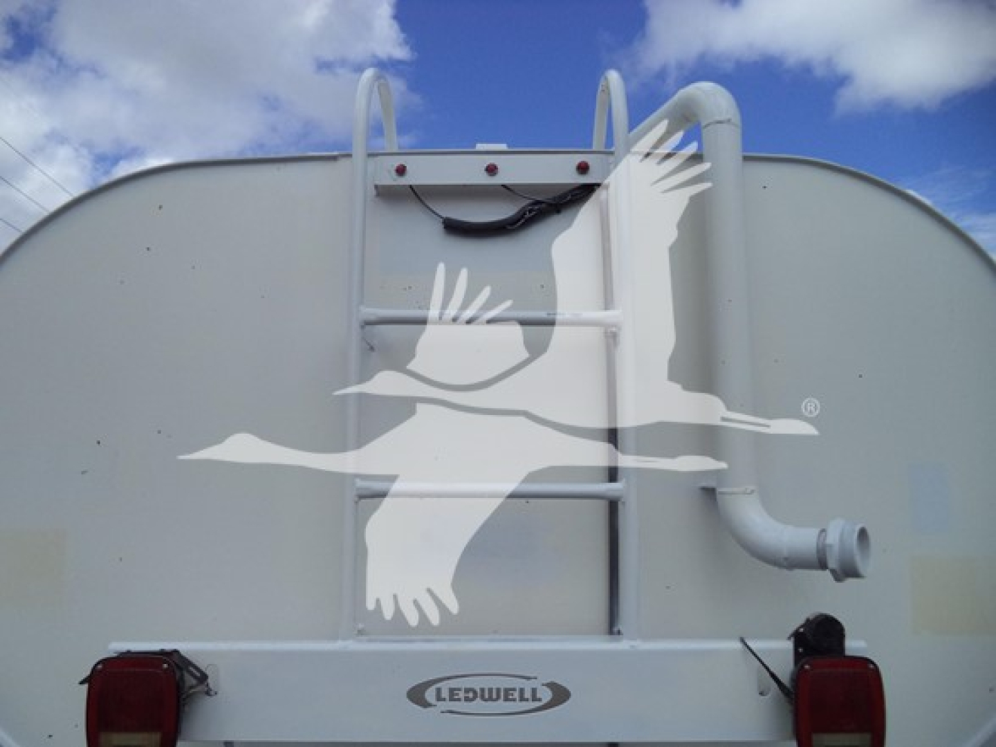 Rear of a white utility truck with a ladder rack, Ledwell logo, and dual red taillights. A large curved pipe extends from the right side.