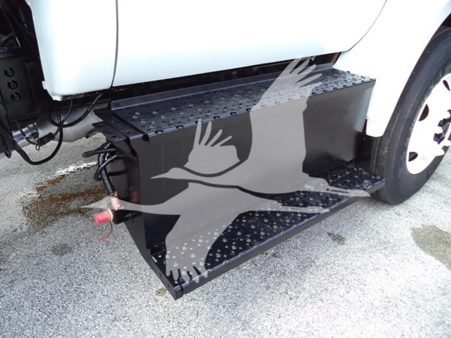 Truck side view showing a large black aluminum running board/step attached to the Ford F650 with perforated tread and a red hitch/connector visible.