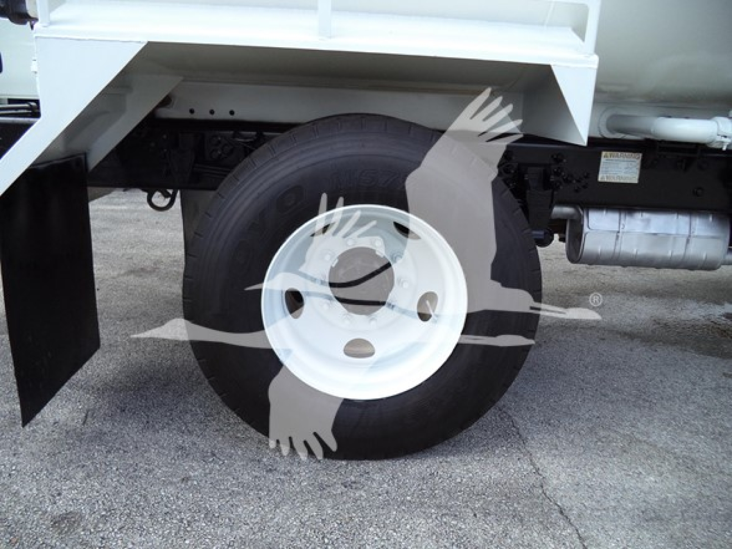 Wheel and front suspension of a Ford F650 truck showing single white steel rim and tire under truck bed side view.