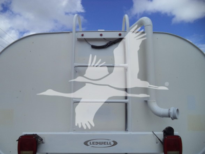 Rear of a white utility truck with a ladder rack, Ledwell logo, and dual red taillights. A large curved pipe extends from the right side.