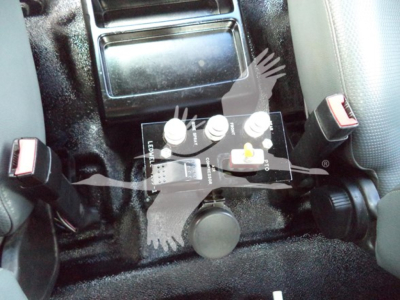 Ford truck interior center console showing control panel with three knobs and switch, cup holder nearby, seat on each side, black textured flooring.