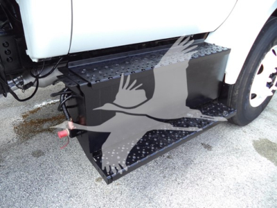 Truck side view showing a large black aluminum running board/step attached to the Ford F650 with perforated tread and a red hitch/connector visible.