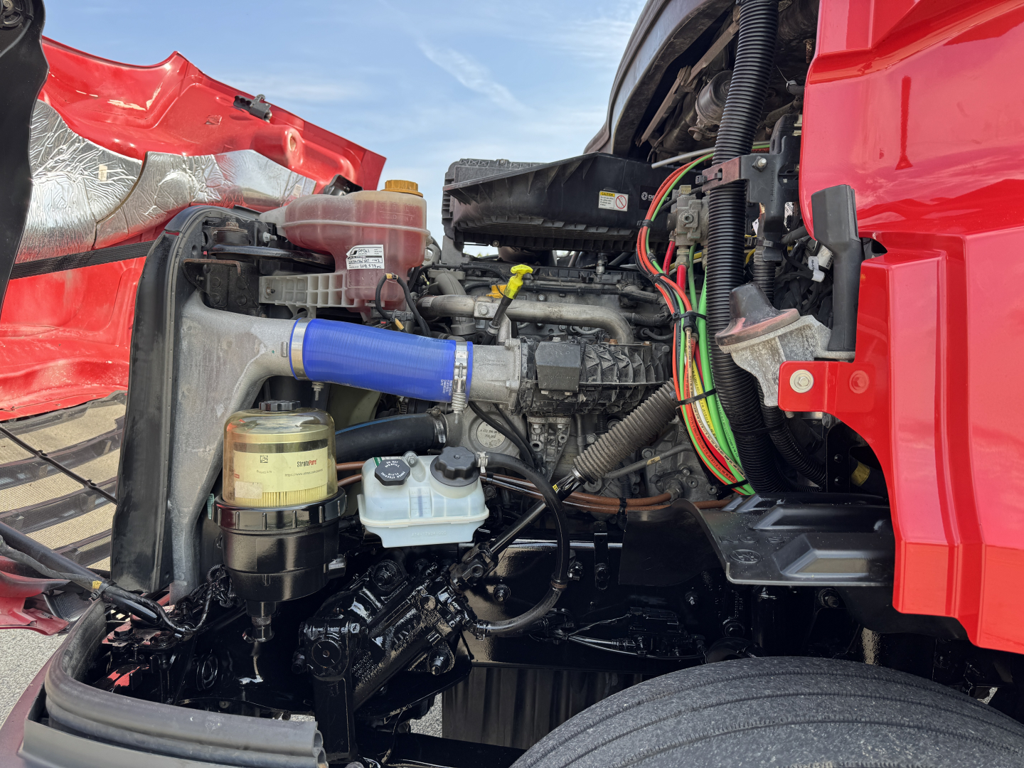 Freightliner Cascadia 116 engine bay showing blue silicone hose, coolant reservoir, fuel/wuel filter, and wiring loom.